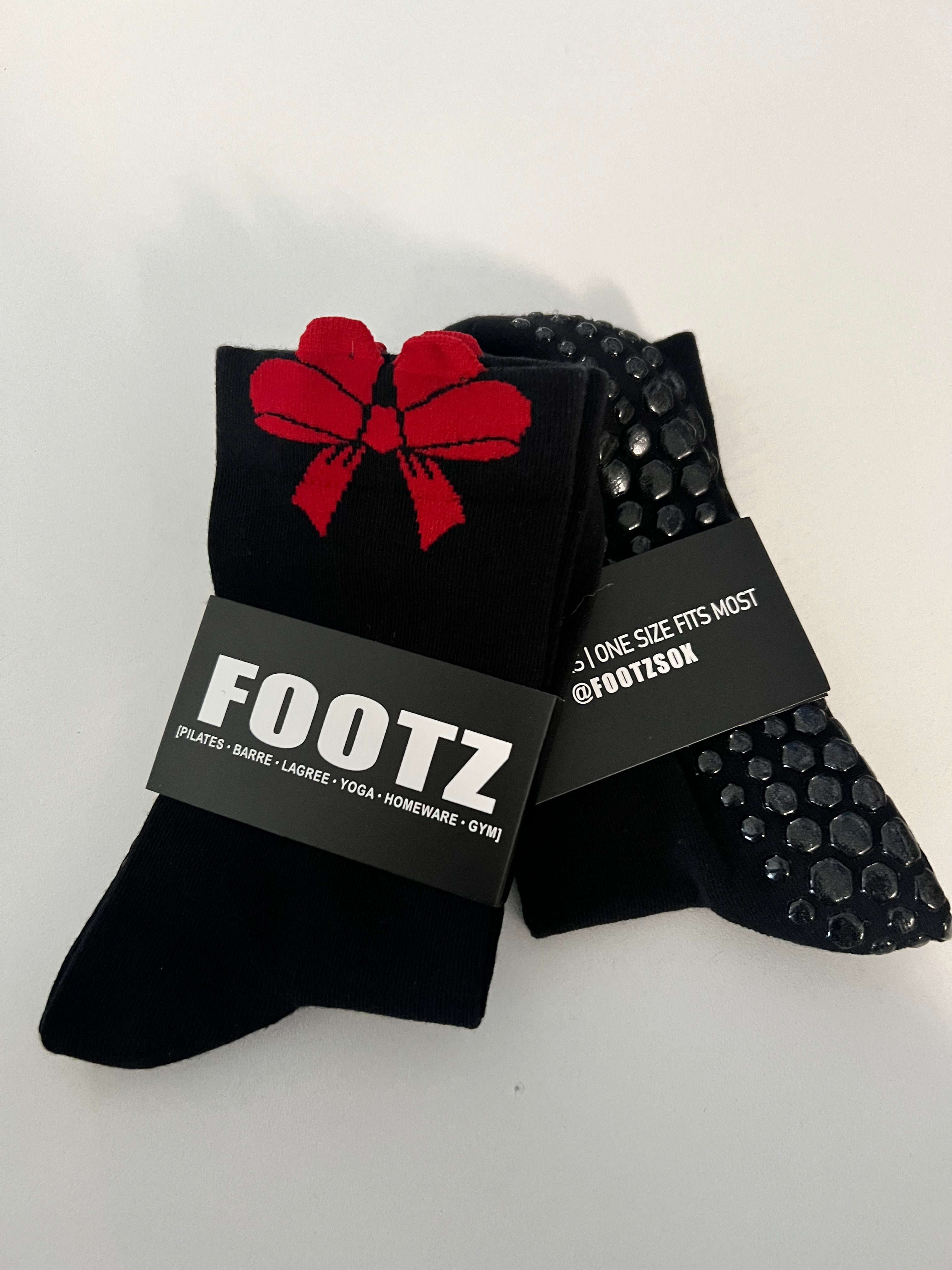 Footz brand socks showcase a black pair adorned with a red bow and another with non-slip grips.
